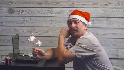 dreamy man in a christmas hat with bengal fire sparkler and laptop in his hands. Falling Money Dollars.