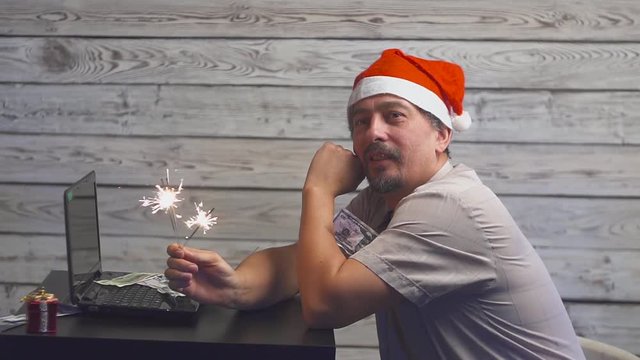 dreamy man in a christmas hat with bengal fire sparkler and laptop in his hands. Falling Money Dollars.