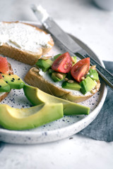 Toasts with avocado, tomatoes and cream cheese on a white plate. Breakfast or lunch concept, high angle view