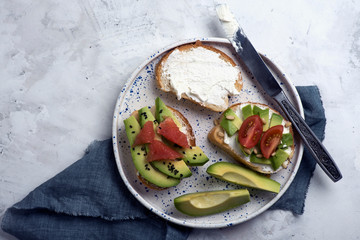 Toasts with avocado, grapefruit. tomatoes and cream cheese on a white plate. Breakfast or lunch concept, Top view