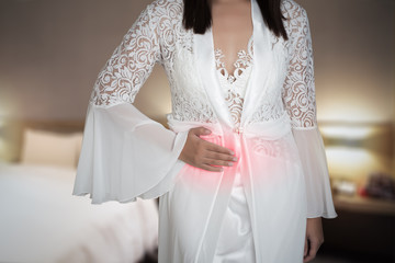 The woman in white silk nightgown and lace robe with stomach ache on the bedroom, inflammatory...