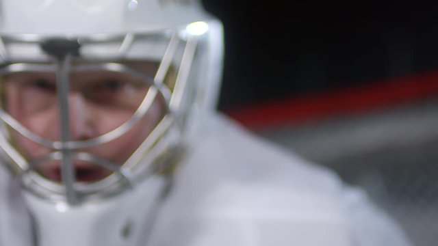 Zoom in close up shot of blue eyed ice hockey player in helmet standing in front of the net and waiting