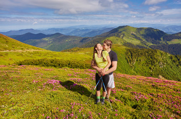 Man and woman standing and hugging on the top of the mountain, summer hike