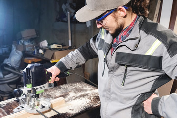 Portrait of a young carpenter joiner with electric milling cutter in the hands of a worker in a home workshop. Starting a business. Craftsman
