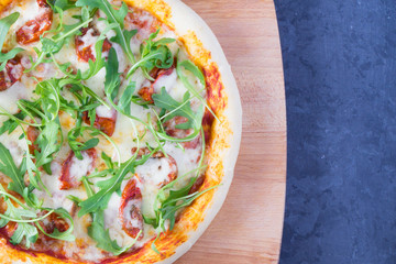 Pizza with dried tomatoes, arugula and mozzarella on a gray-blue dark background with copy space