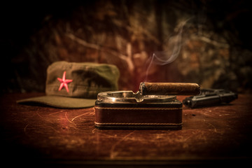 Close up of a Cuban cigar and ashtray on the wooden table. Communist dictator commander table in dark room. Army general`s work table concept. - obrazy, fototapety, plakaty