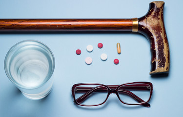 On a blue background are glass glasses, an elderly man's cane and medicines or pills.