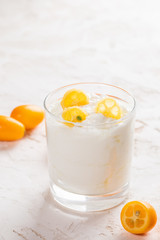 Glass with yogurt with slices of kumquat on white background.