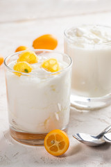 Two glasses with homemade fat yogurt with juicy kumquat  slices and two metal spoons on white background.