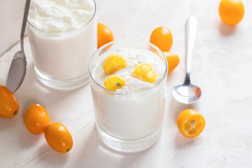 Two glasses with yogurt with kumquat  slices, whole and cut kumquat on white background.