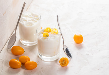Two glasses with yogurt and whole and cut kumquats on white background.