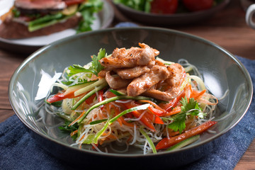 Fresh Asian salad with chicken breast, vegetables,funchosa, cucumbers, tomatoes on wooden background.