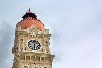 Clock on an urban stone tower against a gray sky with clouds. Copy space