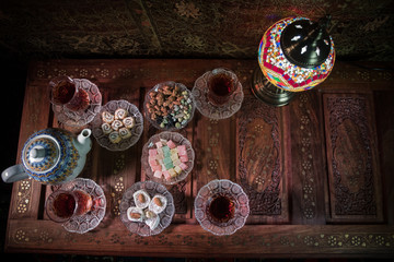 Arabian tea in glass with eastern snacks on vintage wooden surface. Eastern tea concept. Low light lounge interior with carpet. Empty space.