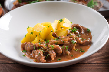 Beef Stroganoff, goulash, with sauce and mushrooms, and boiled potatoes, shot on a dark rustic texture