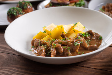 Beef Stroganoff, goulash, with sauce and mushrooms, and boiled potatoes, shot on a dark rustic texture