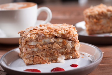 Piece of Napoleon cake on a plate, wooden background. Russian cuisine, layer cake with pastry custard, close-up