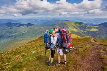 Fototapeta premium Man and woman standing and hugging on the top of the mountain, summer hike with backpacks