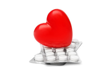 Red heart with pills in blisters on white.