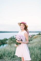  girl in a dress with a hat and flowers near the river