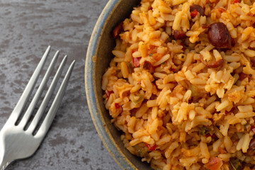 Top close view of a bowl of Mexican rice and beans with a fork to the side on a gray background
