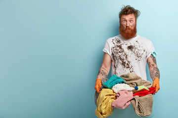 Crazy bearded man crosses eyes, has funny facial expression, dirty clothes and face, carries basin...