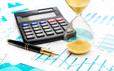 Hourglass on paper financial graphs.