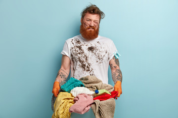 Helpless bearded unshaven man looks unwillingly, has no wish to wash linen, frowns face in...
