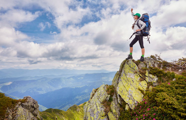 Lady hiker with backpack standing on top of the mountain