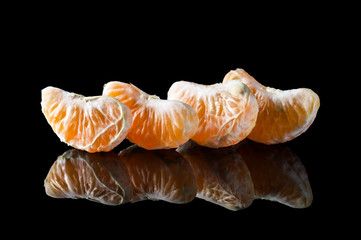 Row of tangerines or mandarins slices on black reflective background.