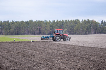 Fototapeta premium A farmer on a tractor prepares the land with a cultivator. Sowing on agricultural fields.