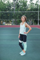 A woman in sports clothes and a yoga mat looks straight at the camera. A woman after a morning workout on the playground. A woman holding a gym mat and practicing yoga.