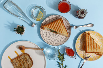 Delicious turkey sandwich on colored plates in the composition of the server table with a glass of water, tomato juice and sauce. Top view. Breakfast concept.