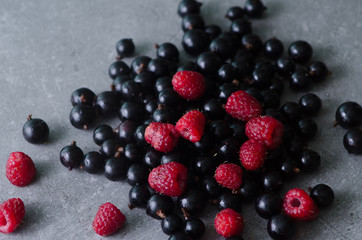 Bunch of fresh raspberries and black currants on a grey table. Close-up view