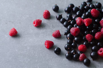 Bunch of fresh raspberries and black currants on a grey surface