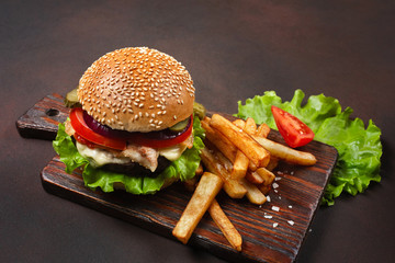 Homemade hamburger with ingredients beef, tomatos, lettuce, cheese, onion, cucumbers and french fries on cutting board and rusty background