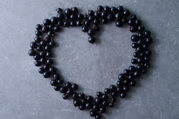 Black currants in a shape of heart on a grey table. Top view, copy space