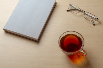 Gray diary, cup of tea, and glasses on a brown table, selective focus