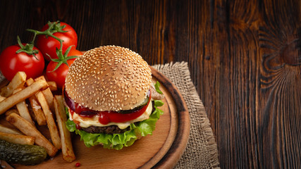 Homemade hamburger close-up with beef, tomato, lettuce, cheese and french fries on cutting board