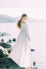 Fototapeta na wymiar Girl in boudoir dress on the lake, standing and smiling. Unity with nature, morning bride in Russia. Beautiful eyes and model appearance