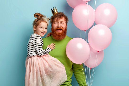 Family, holidays and children concept. Tired red haired father organizes party for daughter, gives balloons, holds small child on hands, come on festive event together, model indoor, have fun
