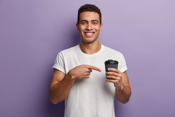 Youngster with toothy smile, wears casual white t shirt, points with fore finger at takeaway...