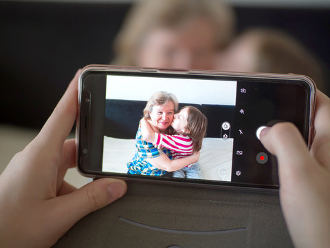 Joyful grandmother and granddaughter hugging at home, making photos on the phone