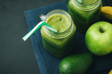 Green, healthy, detox smoothie from avocado, banana, apple in mason jar on blue napkin, dark background, vegetarian food