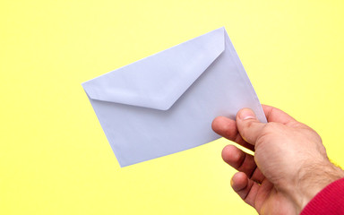 A hand is holding a white envelope on a yellow background.