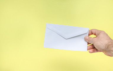 Fototapeta premium A hand is holding a white envelope on a yellow background.
