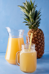 Pineapple juice and fresh tropical fruits  on a blue background. Sweet composition of summer drink. 