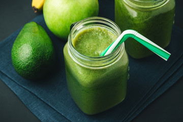 Green, healthy, detox smoothie from avocado, banana, apple in mason jar on blue napkin, dark background, vegetarian food