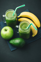 Green, healthy, detox smoothie from avocado, banana, apple in mason jar on blue napkin, dark background, vegetarian food