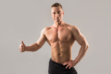 handsome male athlete with muscled muscles on gray background with hand gesture